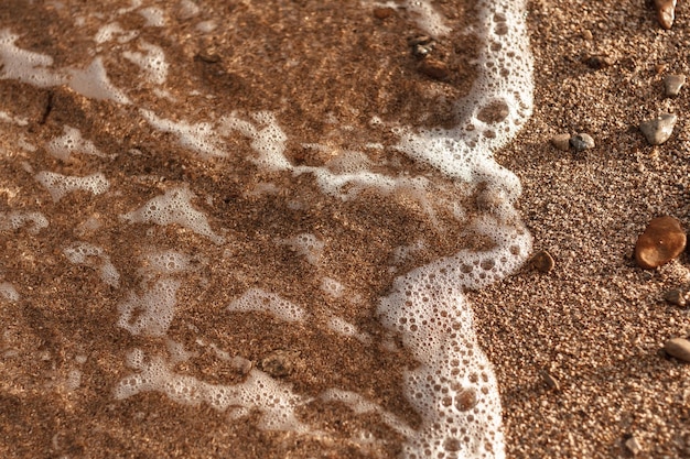 Aproximação de uma onda do mar com espuma do mar e areia grossa