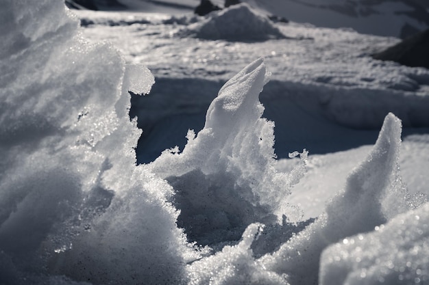 Aproximação de uma parede de neve translúcida derretida contra o pano de fundo das montanhas