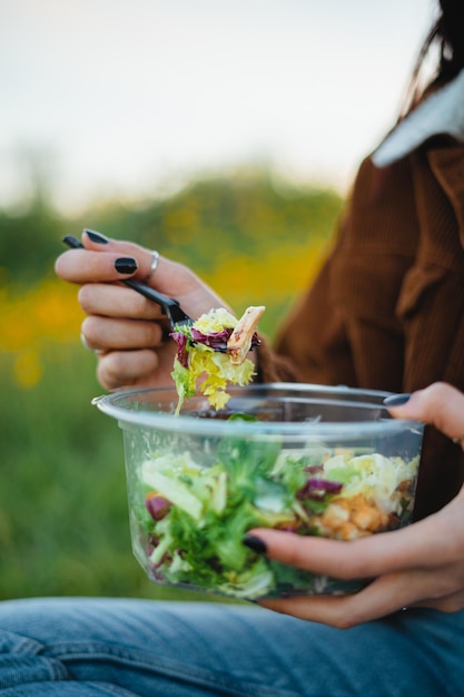 Aproximação de uma tigela de salada Adolescente comendo salada enquanto está sentado na grama cercado por flores amarelas