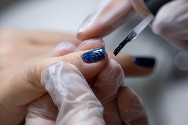 Aproximação de uma unha na qual é aplicado um verniz de gel azul, distribuindo-o com uma escova de manicure sobre a superfície