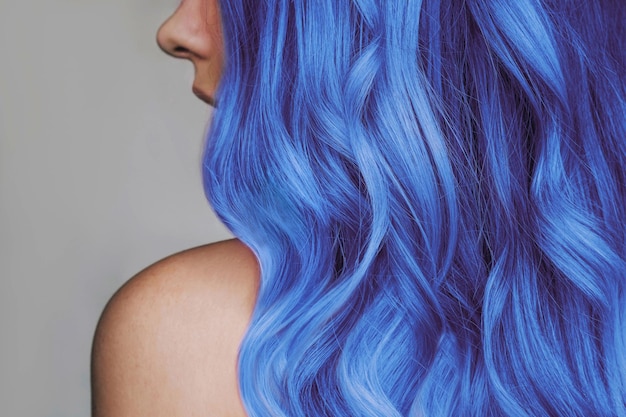 Aproximação do cabelo azul quente ondulado de uma jovem isolada em um fundo cinza Resultado da coloração