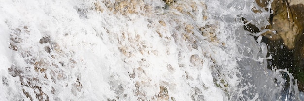 Aproximação do fluxo de cachoeira do rio flui sobre pedras musgosas borbulhando água de cascata com branco