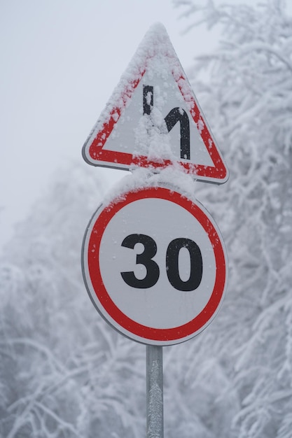 Aproximação do limite de velocidade do sinal de trânsito de advertência 30 km Entrada de automóveis com neve Floresta de inverno após a queda de neve