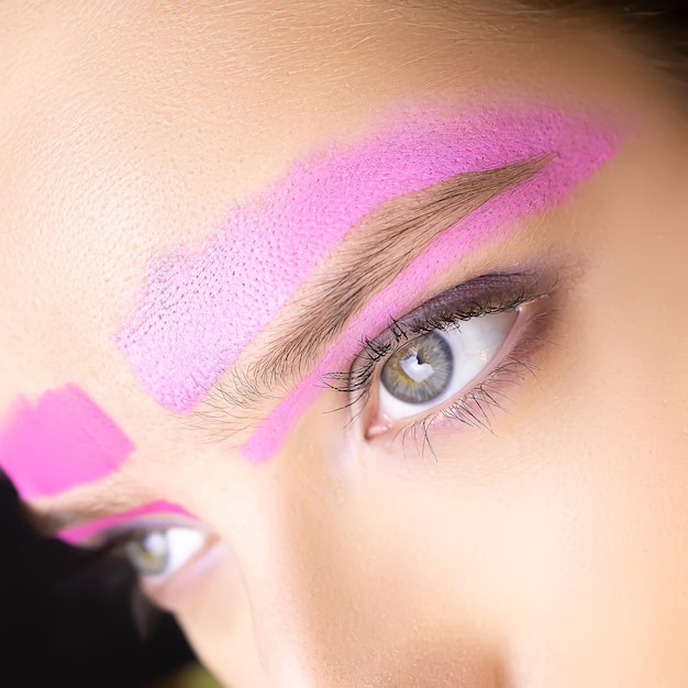 Aproximação do olho aberto do modelo e da sobrancelha em torno da qual é aplicada a pasta corretiva de sobrancelha de cor rosa
