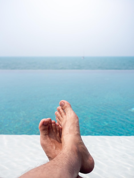 Aproximação do pé do homem na água azul na piscina tropical e vista para o mar Férias de férias estilo vertical de fundo de verão