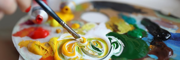 Aproximação do pintor combina cores na paleta de tintas a óleo cremosas no equipamento do pintor de superfície