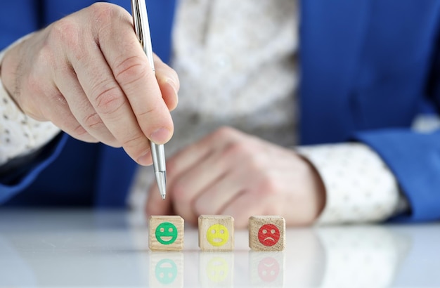 Aproximação do símbolo de rosto de emoção no cubo de madeira bloqueia a mão masculina apontando para emoji verde com caneta