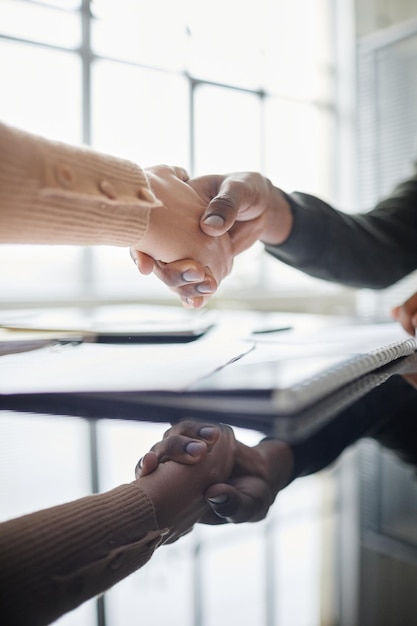 Aproximação vertical de duas pessoas apertando as mãos sobre a mesa de reunião no escritório com reflexo no espelho