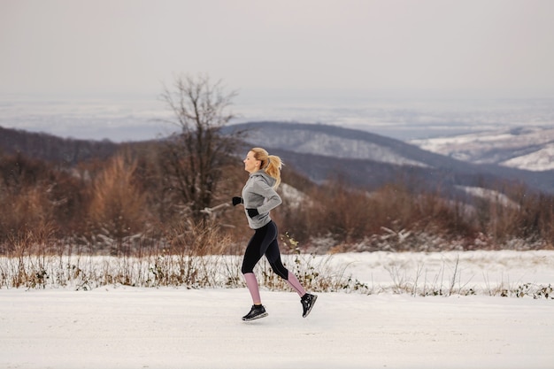 Apta a desportista correndo na neve na natureza no inverno. estilo de vida saudável, exercícios cardiovasculares, preparação física no inverno