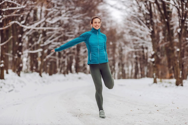 Apta a desportista em pé na neve na floresta e fazendo exercícios de fitness. vida saudável, fitness de inverno