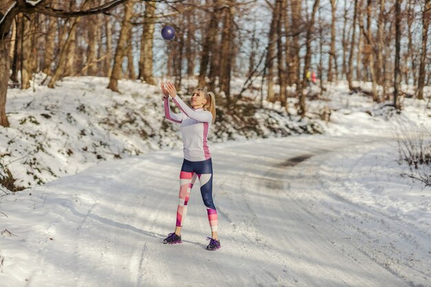 Apta a desportista, jogando uma bola de fitness no ar e fazendo exercícios de fitness. fitness de inverno, vida saudável, fitness ao ar livre