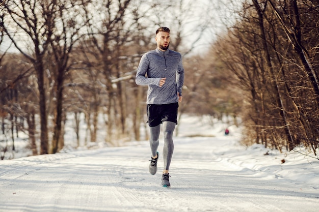 Apta o desportista correndo na natureza na neve no inverno. Estilo de vida saudável, fitness de inverno, clima frio