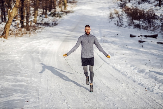 Apta o desportista pulando a corda na natureza em dia de inverno nevado. Fitness de inverno, exercícios cardiovasculares