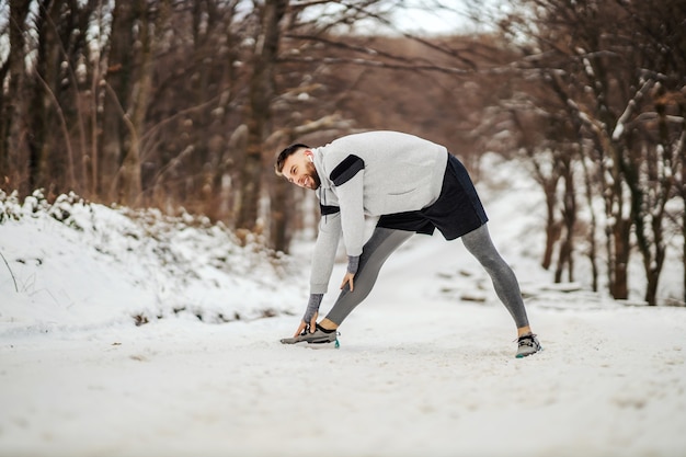Apta o esportista fazendo alongamento e exercícios de aquecimento em pé na natureza em um dia nevado de inverno. Fitness ao ar livre, fitness de inverno, estilo de vida saudável