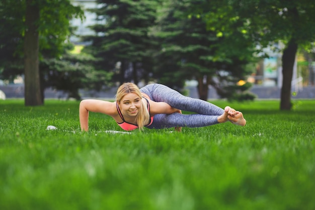 Aptidão, pose de ioga de treinamento de mulher ao ar livre no parque, espaço de cópia. Jovem magro faz exercício. Conceito de alongamento, bem-estar, calma, relaxamento, estilo de vida ativo e saudável