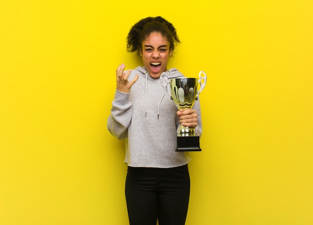 Aptitud joven mujer negra muy asustada y asustada. Sosteniendo un trofeo.