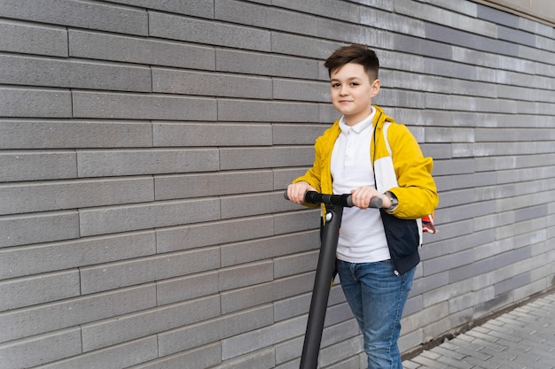 Apuesto adolescente monta en scooter eléctrico cerca de una pared de ladrillos