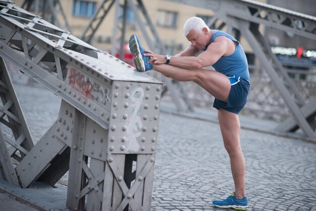 un apuesto anciano estirándose y calentándose antes de hacer ejercicio para trotar a primera hora de la mañana