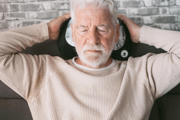 Un apuesto anciano sentado en el sofá con una almohada de masaje detrás de la cabeza con los ojos cerrados