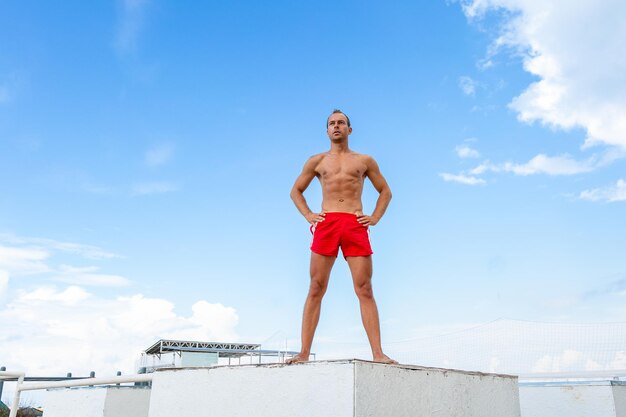 Apuesto atleta joven sin camisa se encuentra en una roca contra el cielo ejercicio de yoga al aire libre