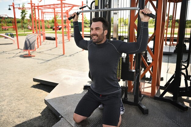 Un apuesto atleta de mediana edad practica deportes, sacude los hombros y los músculos de la espalda en un simulador estacionario en un campo atlético