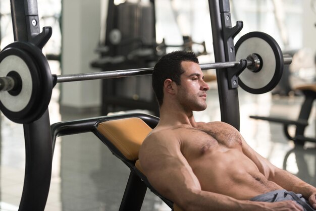 Apuesto y atractivo joven con cuerpo musculoso sentado en un banco y relajándose en el gimnasio