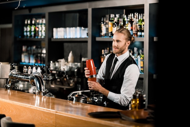 Apuesto barman mezclando bebida en coctelera