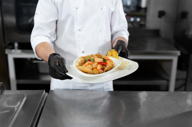 Un apuesto chef sostiene un plato de mariscos preparado en sus manos