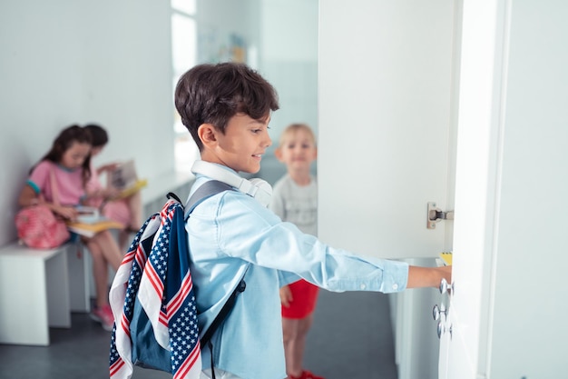 Apuesto colegial con mochila de pie cerca del casillero