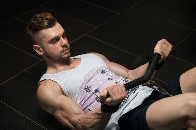 Apuesto culturista musculoso en camiseta haciendo ejercicio de peso pesado para bíceps en la máquina con cable en el gimnasio