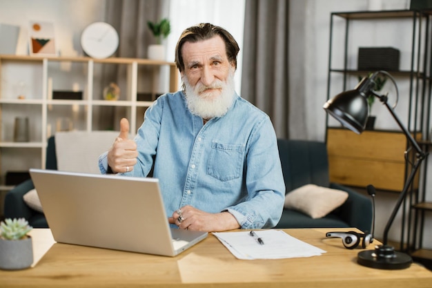 Apuesto desarrollador de software senior en ropa casual escribiendo en la computadora portátil mientras está sentado en el lugar de trabajo