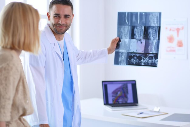 Foto el apuesto doctor está hablando con una joven paciente y tomando notas mientras está sentado en su oficina