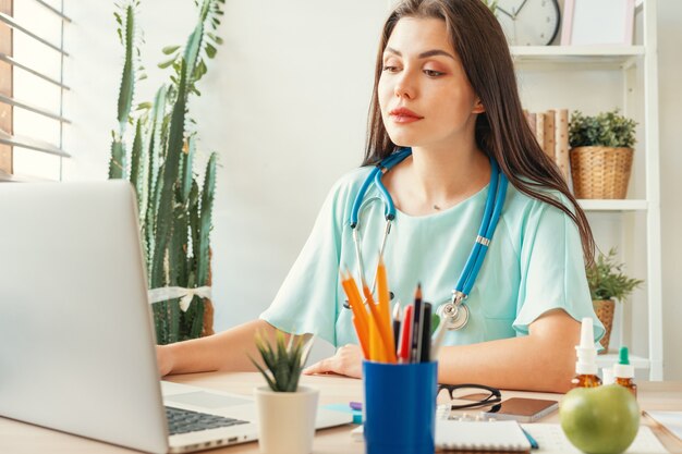 Apuesto doctor mujer sentada en su mesa en el consultorio médico