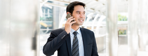 Apuesto empresario asiático llamando por teléfono inteligente mientras caminaba por la ciudad