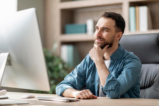 Apuesto empresario masculino sentado en el lugar de trabajo con expresión facial pensativa