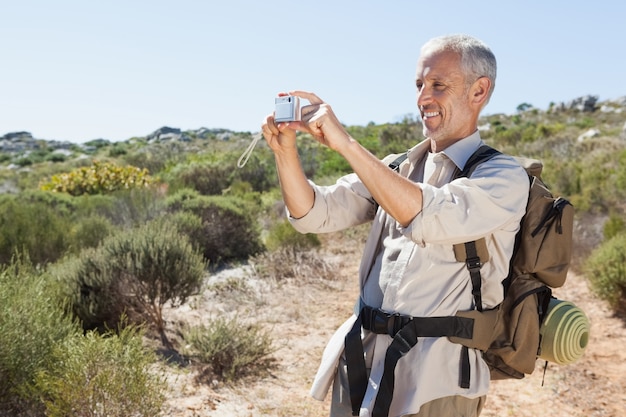 Apuesto excursionista tomando una foto en el campo