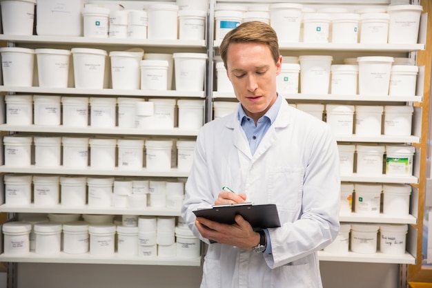 Foto apuesto farmacéutico escribiendo en portapapeles