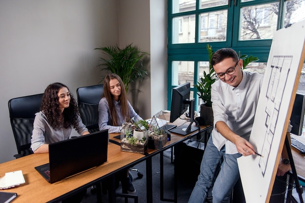 Foto el apuesto gerente de la empresa con gafas explica las tareas laborales de sus empleados. gente creativa o concepto de negocio de publicidad. trabajo en equipo. jóvenes hermosas personas trabajando juntos en la oficina.