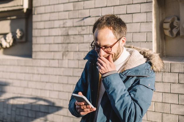 Apuesto hombre adulto con barba mirando al teléfono inteligente y riendo Concepto de emociones agradables