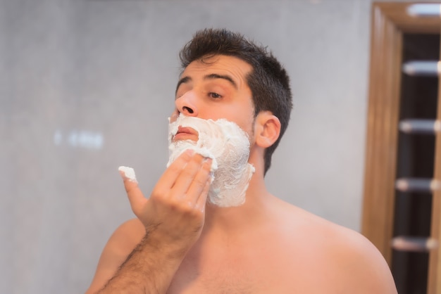 Apuesto hombre afeitarse la barba en el baño