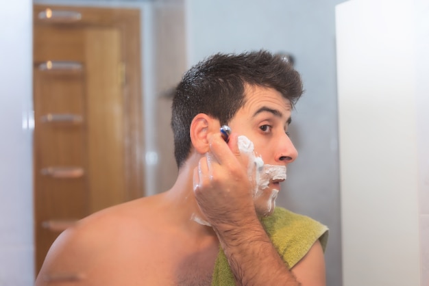 Apuesto hombre afeitarse la barba en el baño