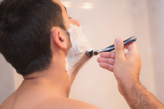 Apuesto hombre afeitarse la barba en el baño