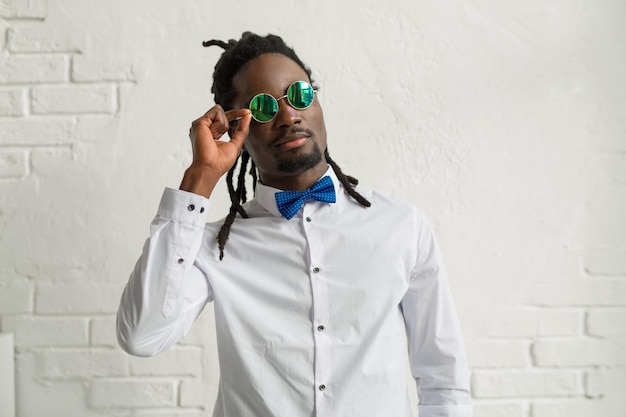 Apuesto hombre africano con rastas en camisa blanca y gafas de sol