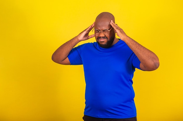 Apuesto hombre afro brasileño con gafas camisa azul sobre fondo amarillo con dolor de manos en la frente dolor de cabeza dolor de cabeza migraña frustración