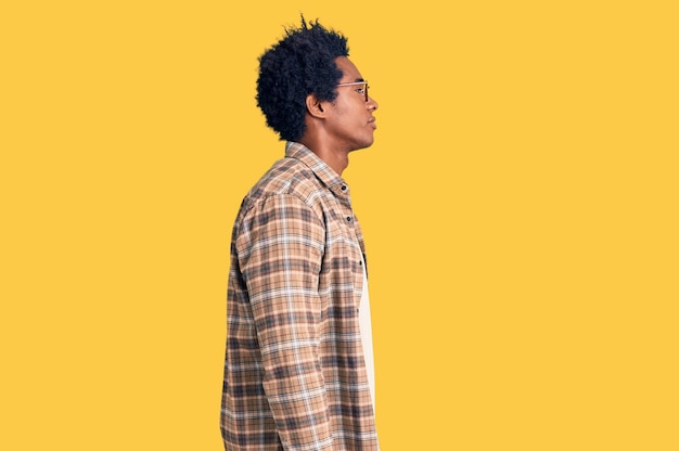 Un apuesto hombre afroamericano con cabello afro vestido con ropa casual y anteojos mirando hacia un lado, pose de perfil relajado con rostro natural y sonrisa segura.