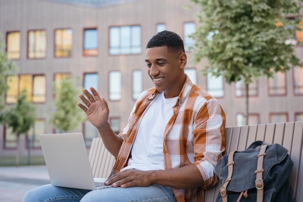 Apuesto hombre afroamericano sonriente independiente usando computadora portátil con videollamada