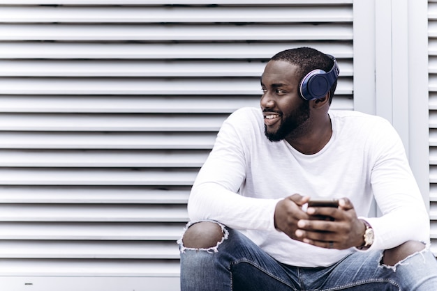 Apuesto hombre afroamericano vistiendo ropa casual en la ciudad moderna escuchando música con auriculares
