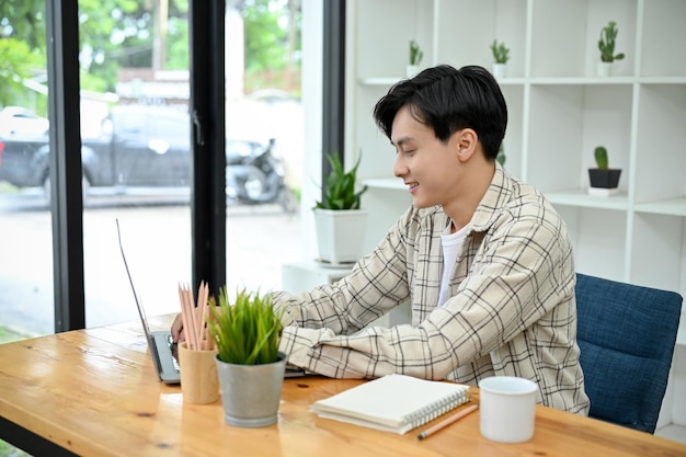 Un apuesto hombre asiático en el espacio de coworking de la cafetería usando una computadora portátil