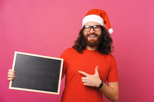 Un apuesto hombre barbudo apunta a una pizarra en blanco para un mensaje de Navidad