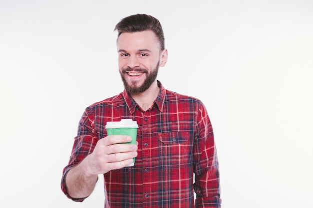 Un apuesto hombre barbudo bebe café de un vaso de papel Café para llevar Concepto de cafetería Cafetería Buenos días Un chico feliz disfruta de un té caliente fresco Un barista sonriente le ofrece una bebida